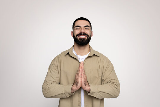 A cheerful man with a neat beard and a bright smile makes a prayer gesture