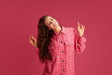 Elegant, beautiful young woman in stylish checkered shirt dancing, having fun against pink studio background. Relaxation. Concept of youth, lifestyle, casual fashion, human emotions