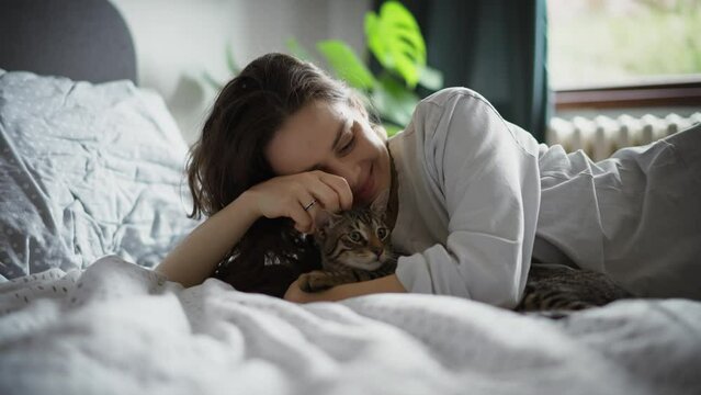 A young Caucasian woman hugging her cute grey cat while lying in bed in the morning