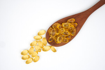 Wooden spoon full of golden fish oil supplement capsules concept background