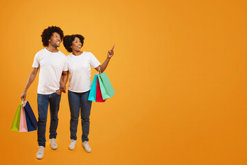 Excited young black couple shopping together, pointing at copy space