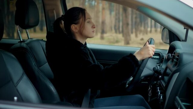 Woman driving vehicle at forest. Female driver beginner practicing driving after getting licence on empty place. Female learn driving and traveling alone. Shooting from outside