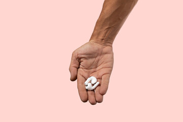 Male hand holding white earbuds on pink background.