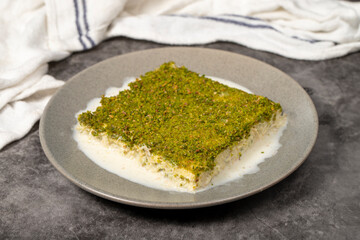 Cold kadayif with pistachio. Milk kadayıf dessert with pistachios on a dark background. Local name soğuk kadayıf tatlısı. Close up