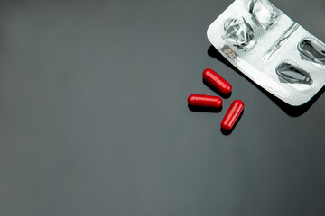 three red capsules for treatment with an empty package on a dark background