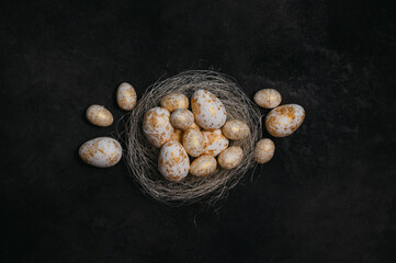 golden and white eggs in the nest on black rustic background. Homemade layout. Easter festive flat lay. Low key photo