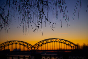 Fototapeta na wymiar A beautiful sunrise scenery with iron bridge over the frozen river Daugava in Latvian capital city Riga. Winter landscape of Northern Europe.