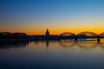 A beautiful sunrise scenery with iron bridge over the frozen river Daugava in Latvian capital city Riga. Winter landscape of Northern Europe.