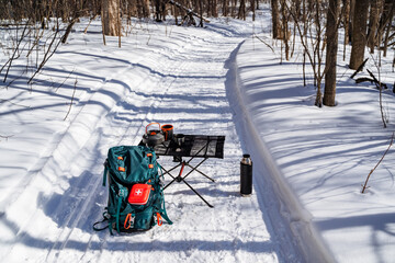 Camping equipment stands on the snow in the winter forest, camping in nature, dishes for food, a backpack with a first aid kit, a thermos with tea.