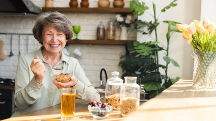 Healthy eating dietary habits concept. Caucasian senior old elderly woman grandmother eating breakfast, oats cereals with berries and apple juice
