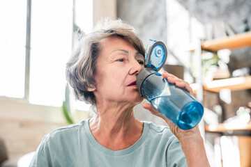 Senior old grandmother woman drinking water from bottle after training home workout yoga class....