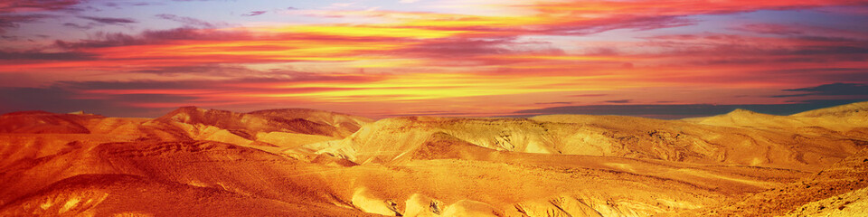 Mountainous desert with colorful cloudy sky. Judean desert in Israel at sunset. Horizontal banner
