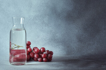 Elegant Water Carafe with Red Grapes on Textured Grey Background