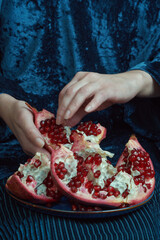 Person delicately separating pomegranate seeds over a blue velvet backdrop. Close-up shot with rich...