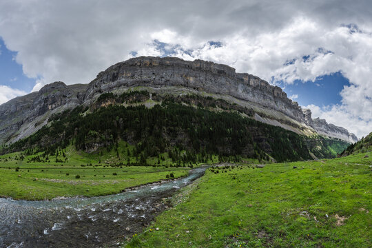 A breathtaking panoramic view of the lush Valle de Ordesa with a flowing river, under the towering cliffs of the Parque Nacional de Ordesa y Monte Perdido in Huesca