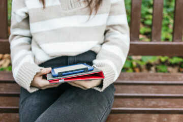 Holding notebook with phone and pen while sitting on bench