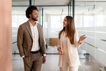 In a modern office corridor, an African-American businessman and his colleague are engaged in a...