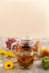 Red tea with herbs in glass teapot on brown concrete. Side view, selective focus.