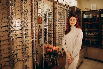 A young woman chooses glasses in an optical store. Stand with glasses. Vision correction. Woman in...