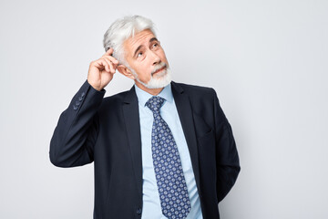 Mature businessman in suit making thinking gesture against a white background.