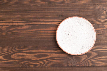 Empty white ceramic plate on brown wooden background. Top view, copy space