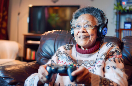 Portrait of a happy senior woman playing video games. Elderly woman with headphones playing on console at home sitting on the sofa. Concept of new forms of fun for older people. 