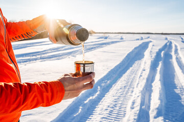 A thermos with tea on the background of snow, the glare of the sun shines into the camera, hot tea...