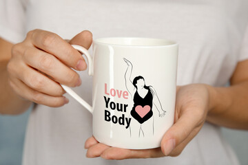 Woman holding cup with image of figure of plus-size model in bodysuit, heart and phrase Love Your...