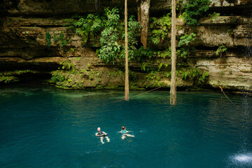 turquoise crystal clear water of  San Lorenzo Oxman cenote lake with waterfall dripping from top of the opening in Yucatan Mexico