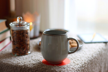 Cup of tea or coffee, stack of books, e-reader, glasses, various cookies, almonds, orange juice and lit candles on the table. Hygge at home. Selective focus.
