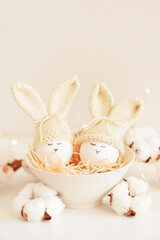 Easter eggs in crochet knitted hats with rabbit ears in nest. Easter celebration concept