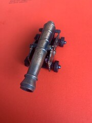Old miniature canon isolated on red. - obrazy, fototapety, plakaty