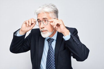 Confident senior businessman adjusting glasses, isolated on grey background.