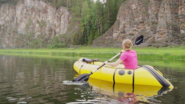 Woman traveler swims in boat on mountain river surrounded by high mountains. Girl kayak rafting rowing leisurely paddle along calm river. Packrafting