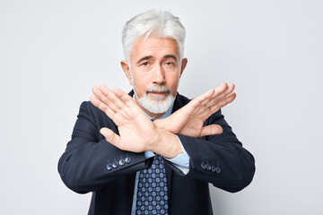 Senior businessman making stop gesture with arms crossed, signaling denial or restriction
