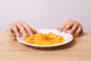 Children's hands are visible from under the table, trying to take potato chips from the table.