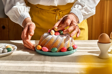 Female hands decorating Easter cake with small colorful chocolate eggs. Anonymous woman making...