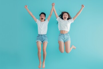 Playful energetic Asian couple in summer beach casual clothes jumping in front of a light blue studio backdrop