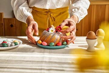 Female hands decorating Easter cake with small colorful chocolate eggs and daisy flowers. Anonymous woman making traditional easter cake or sweet bread with topping. Easter treat.