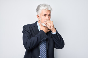 Portrait of elderly man is sick on white background, coughs into his fist, has cold, flu