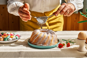 Female hands sprinkles Easter cake with icing sugar through sieve. Anonymous woman making traditional easter cake or sweet bread with topping. Easter treat.