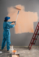 Obraz premium Rear view of a woman painter painting a wall with a paint brush. Home renovation concept.