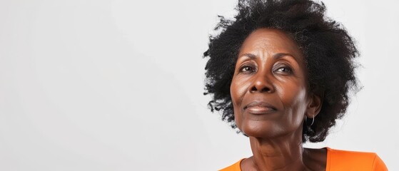 A portrait of a senior African woman gazing upwards, her expression a blend of wisdom and introspection. The subtle orange attire contrasts with her dignified grey hair.
