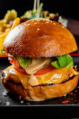 A gourmet burger with melted cheese, bacon, onions, lettuce, and sauce on a sesame seed bun, served on a black plate
