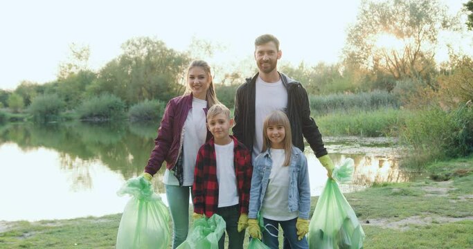 Portrait of family with children which standing in front of camera with rubbish bags after cleaning lake's territory