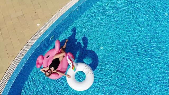  Woman with unicorn and flamingo pool float in pool. Enjoying summer vacations from above. Aerial top view from drone. Summer relax