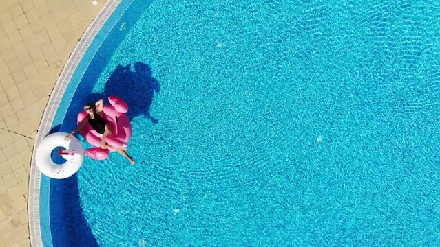 Woman with unicorn and flamingo pool float in pool. Enjoying summer vacations view from above. Aerial top view from drone. Summer relax.