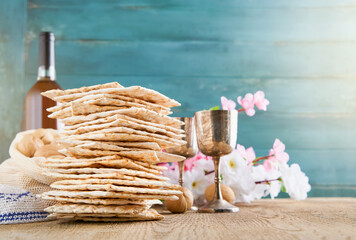 Passover celebration concept. Matzah, red kosher and walnut on wooden vintage table in front of spring blossom tree garden and flowers landscape with sun rays with copy space. Mock up.