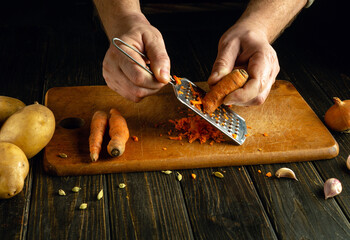 A cook grates raw carrots to prepare a vegetable lunch. Low key concept of the process of preparing...