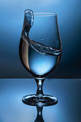 splash of liquid, water in a glass goblet with background illuminated with colored light
